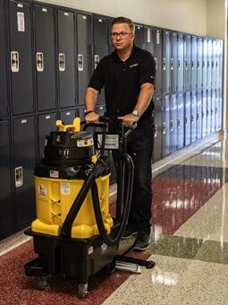 A worker using a cleaning machine in a school hallway.